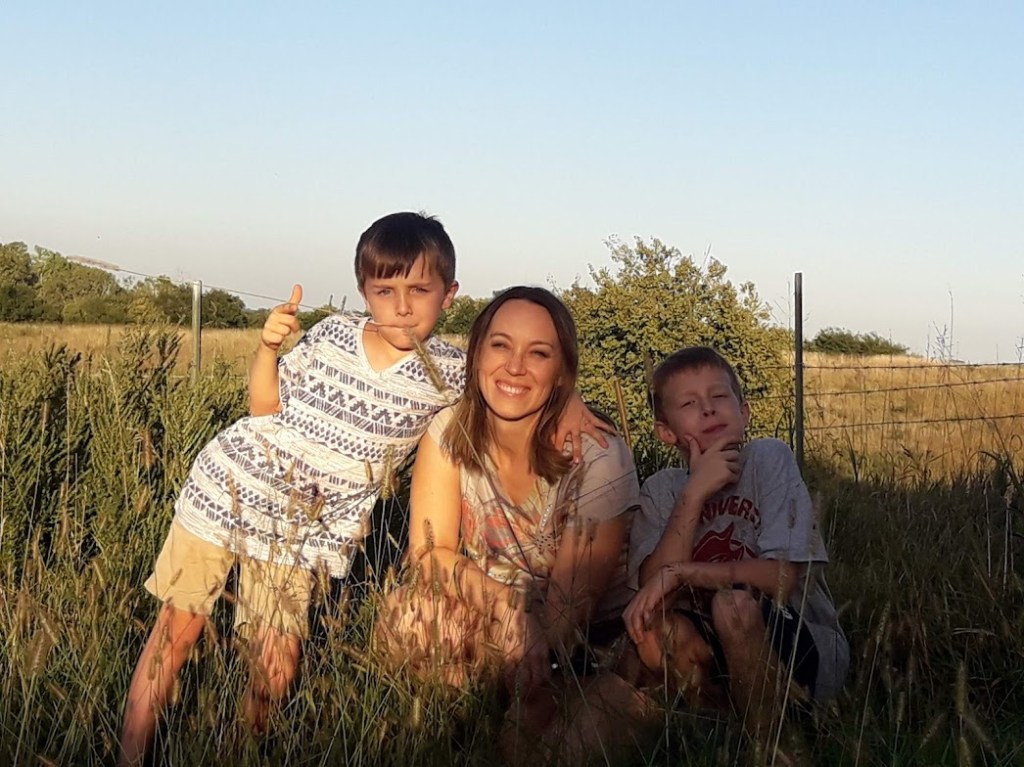 A woman and two boys posing together in a grassy field during sunset.